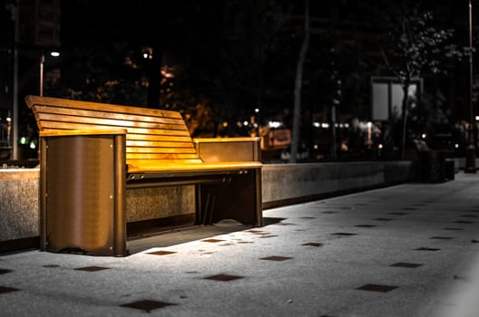 Lit bench on sidewalk at night.