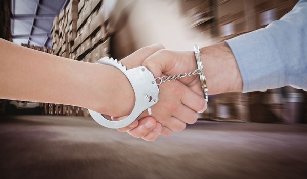 Handcuffed business people shaking hands against worker with fork pallet truck stacker in warehouse