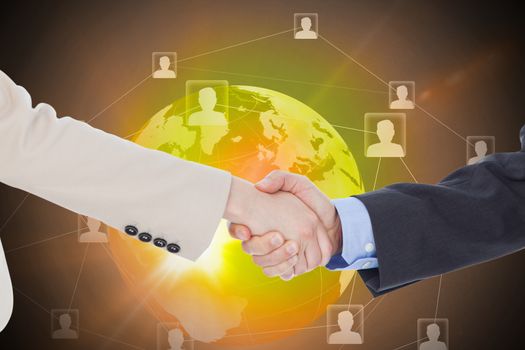 Smiling business people shaking hands while looking at the camera against global technology background