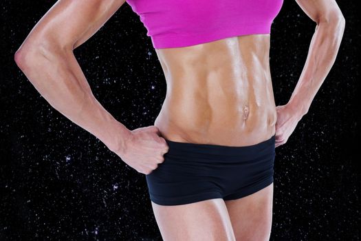 Female bodybuilder posing with hands on hips mid section against black background