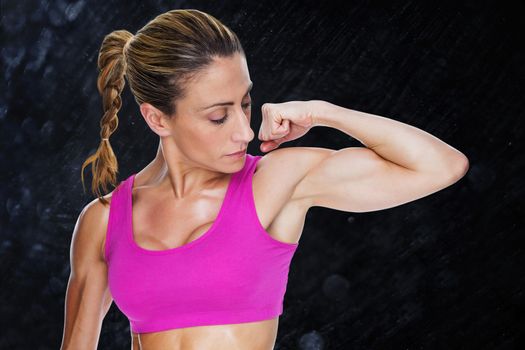 Female bodybuilder flexing bicep in pink sports bra against black background