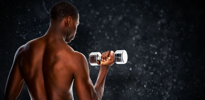 Rear view of a fit shirtless young man lifting dumbbell against black background