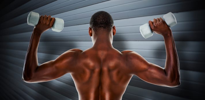 Rear view of a fit shirtless man lifting dumbbells against grey shutters