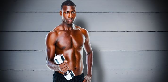 Portrait of a fit shirtless young man lifting dumbbell against painted blue wooden planks