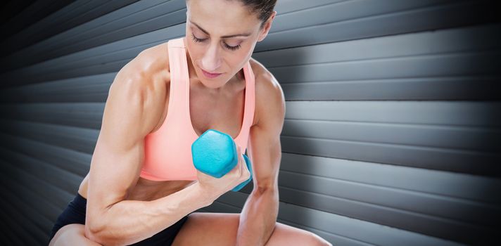 Strong woman doing bicep curl with blue dumbbell against grey shutters