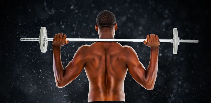 Rear view of a fit shirtless man lifting barbell against black background