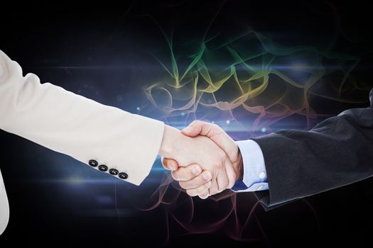 Smiling business people shaking hands while looking at the camera against black background with spark