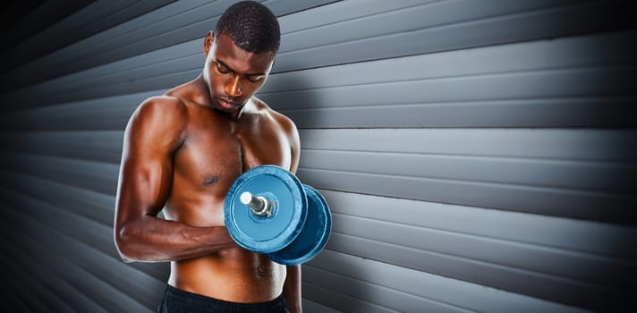 Determined fit shirtless young man lifting dumbbell against grey shutters