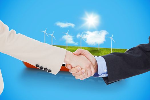 Smiling business people shaking hands while looking at the camera against wind turbine field in an energy saving battery