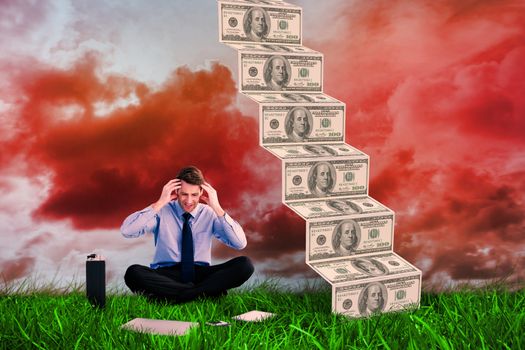 Businessman sitting on the floor with headache against green grass under red cloudy sky