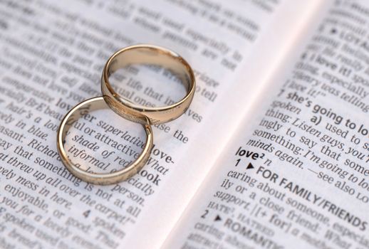 Wedding rings on a dictionary page showing love definition,  close up