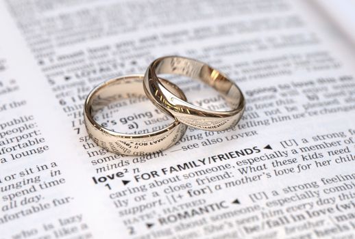 Wedding rings on a dictionary page showing love definition,  close up