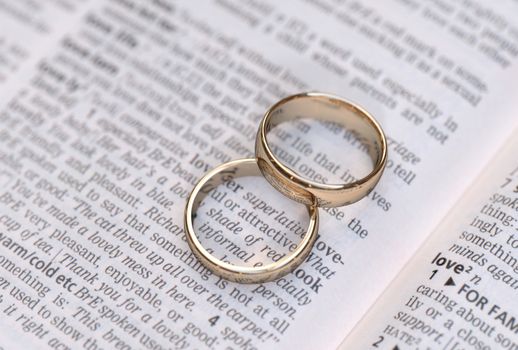 Wedding rings on a dictionary page showing love definition,  close up
