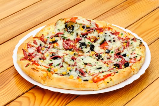 Whole pizza with cut pepperoni, black olives, corn, cheese and pickled cucumbers