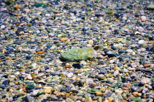 Sea multicolored pebbles, gravel beach in sunlight, selective focus, background