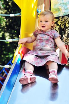 Little baby girl sliding on playground in the park 