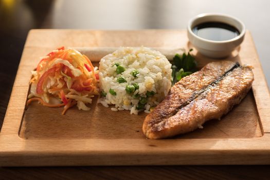 Grilled salmon with rice and vegetables at wooden table