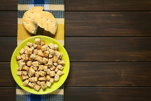 Overhead shot of freshly toasted homemade croutons made of wholegrain bread, photographed on dark wood with natural light