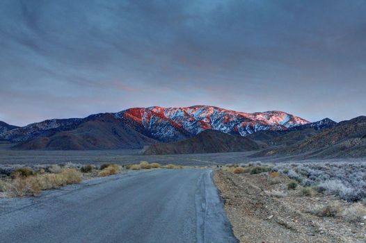 A lonely road toward a snow covered mountain in the desert.