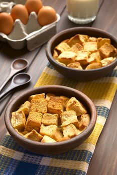 Two rustic bowls of bread pudding made of diced stale bread, milk, egg, cinnamon, sugar and butter, photographed with natural light (Selective Focus, Focus one third into the first bread pudding)