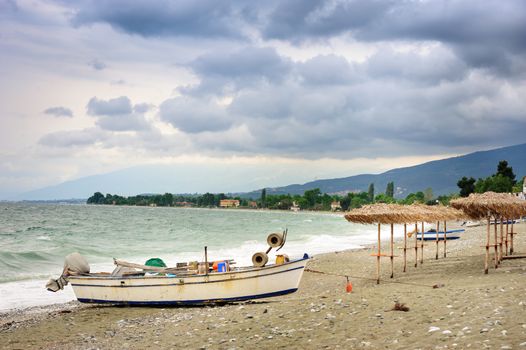 Fisher's boat and reed umbrellas on the sea beach 