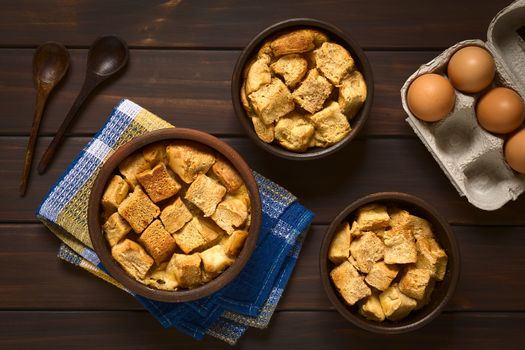 Overhead shot of three rustic bowls of bread pudding made of diced stale bread, milk, egg, cinnamon, sugar and butter, photographed on dark wood with natural light