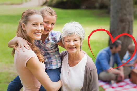 Grandmother mother and daughter with family in background at park against heart