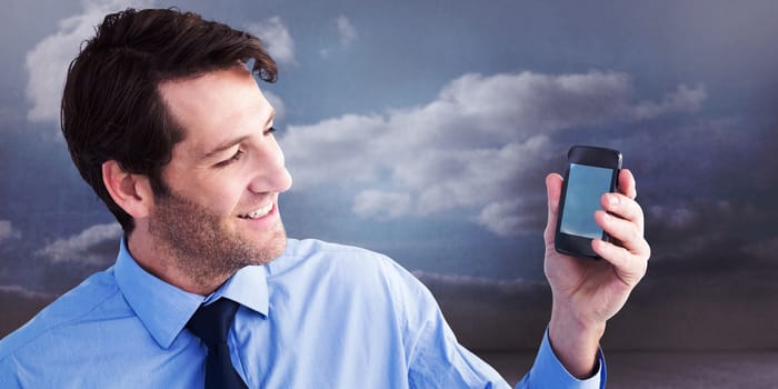 Smiling businessman showing smartphone to camera against clouds in a room