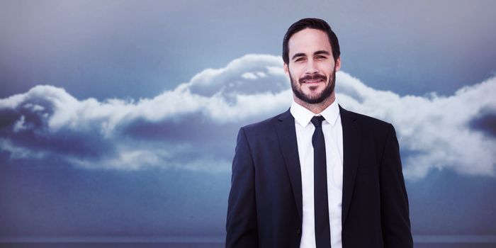 Smiling businessman in suit standing with hands in pockets against clouds in a room