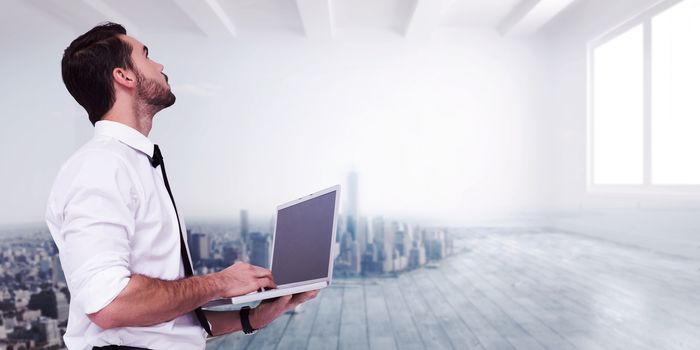 Sophisticated businessman standing using a laptop  against city scene in a room