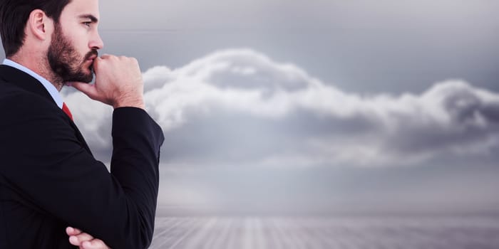 Thinking businessman standing with hand on chin against clouds in a room