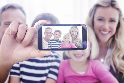 Hand holding smartphone showing against portrait of a smiling family sitting on sofa