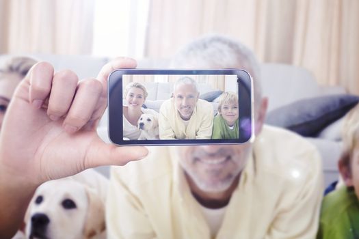 Hand holding smartphone showing against happy parents with their children and puppy on floor