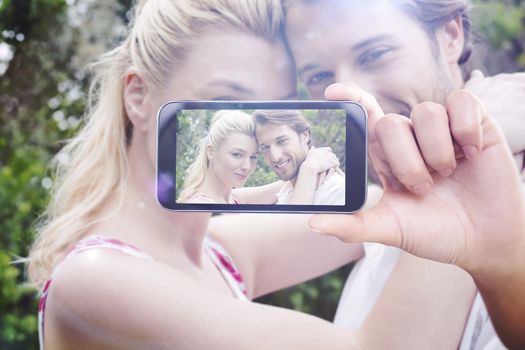 Hand holding smartphone showing against cute couple standing outside hugging smiling at camera