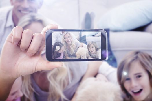 Hand holding smartphone showing against laughting family with their pet yellow labrador on the rug