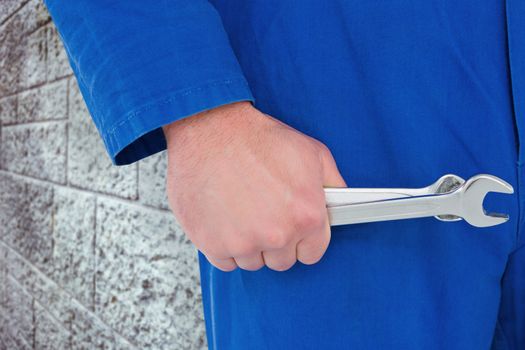 Mechanic holding spanners on white background against grey brick wall