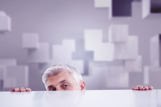 Businessman peeking over desk against abstract white room