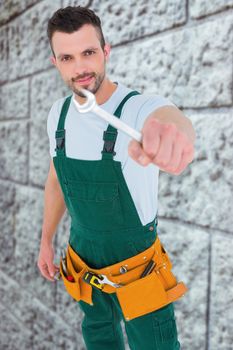 Carpenter showing wrench  against grey brick wall