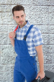 Repairman carrying toolbox while looking asway against grey brick wall