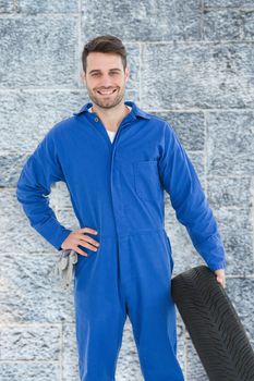 Smiling male mechanic holding tire against grey