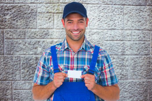 Portrait of happy handyman holding visiting card against grey brick wall