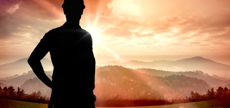 Builder in safety gear against sun shining over mountains