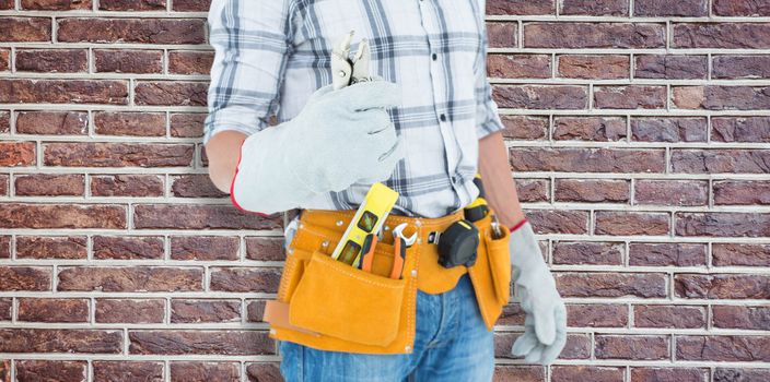 Technician with tool belt around waist holding pliers against red brick wall