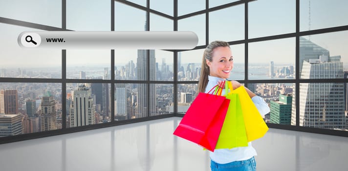 Smiling blonde holding shopping bags against room with large window showing city