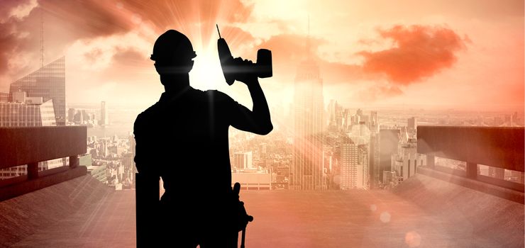 Carpenter showing thumbs up while holding drill machine against sun shining over road and city