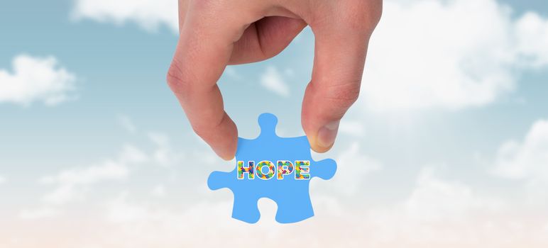 Hand holding jigsaw piece against blue sky