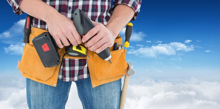 Male repairman holding drill machine against bright blue sky with clouds