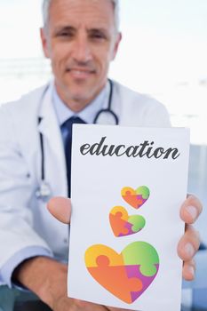 The word education and portrait of a male doctor showing a blank prescription sheet against autism awareness heart