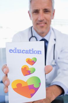 The word education and portrait of a male doctor showing a blank prescription sheet against autism awareness heart