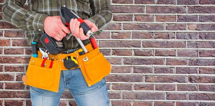 Manual worker holding gloves and hammer power drill  against red brick wall